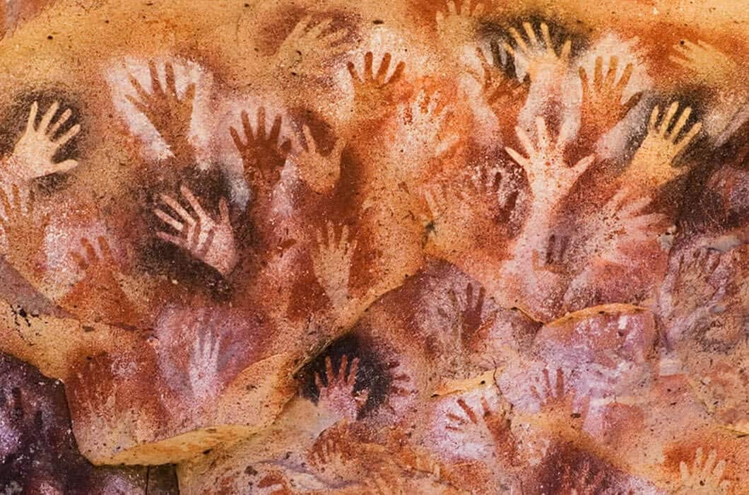 Cave wall in Patagonia covered with numerous hand stencils in shades of brown, red, and white, overlapping to create a layered pattern—an unforgettable travel experience and one of the top things to do in the region.