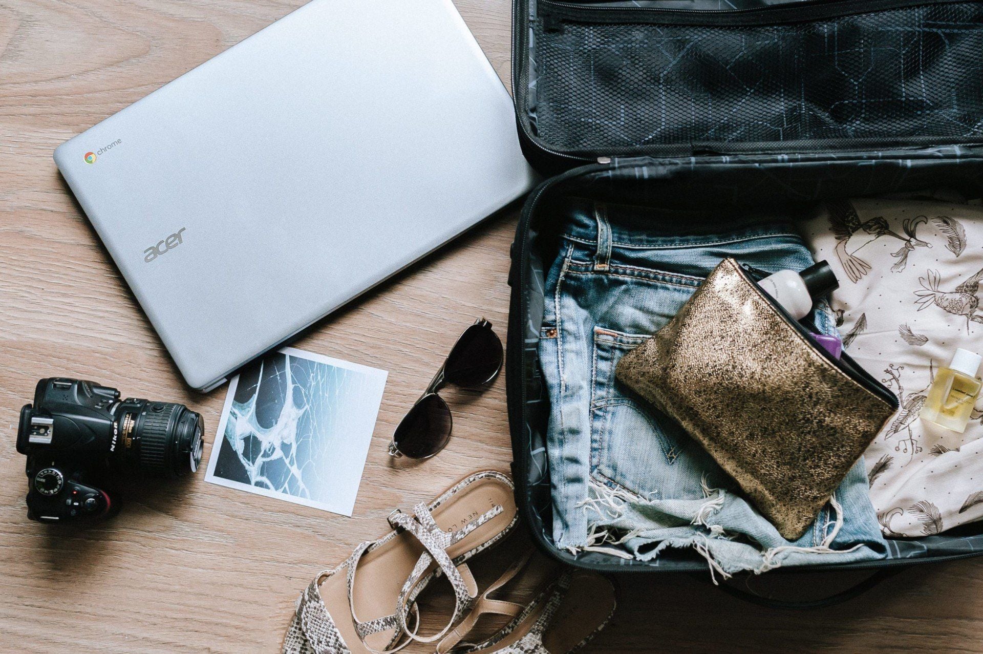 Open suitcase on the floor with folded clothes, a gold pouch, toiletries, sunglasses, a laptop, camera, printed photo, sandals, and adapters for electrical outlets—everything ready for an adventure in South America.