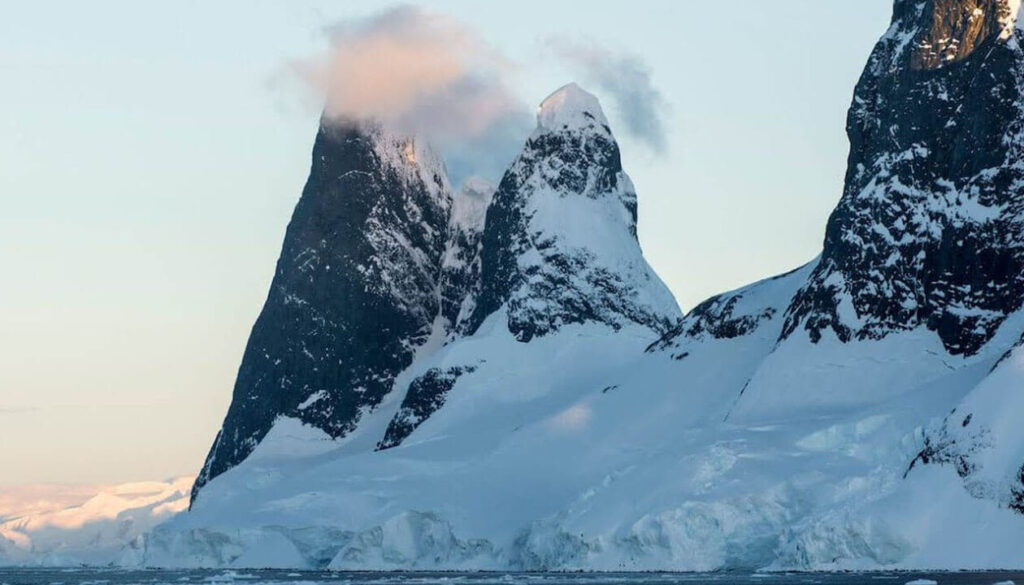 Two steep, snow-covered mountain peaks rise above an icy landscape, with clouds partially covering the taller peak under a pale sky—an iconic view for those visiting Antarctica or planning their next Antarctica travel adventure.