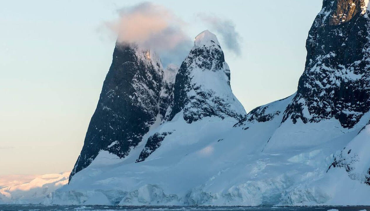 Two steep, snow-covered mountain peaks rise above an icy landscape, with clouds partially covering the taller peak under a pale sky—an iconic view for those visiting Antarctica or planning their next Antarctica travel adventure.