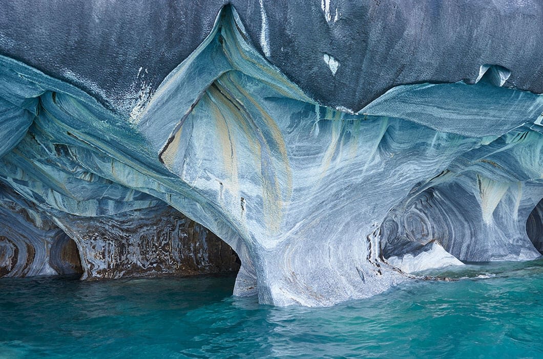 Marble caves with swirling blue, gray, and white patterns rise above turquoise water, creating arching formations and smooth, sculpted surfaces—an unmissable sight for anyone exploring Patagonia or looking for unique things to do in Patagonia.
