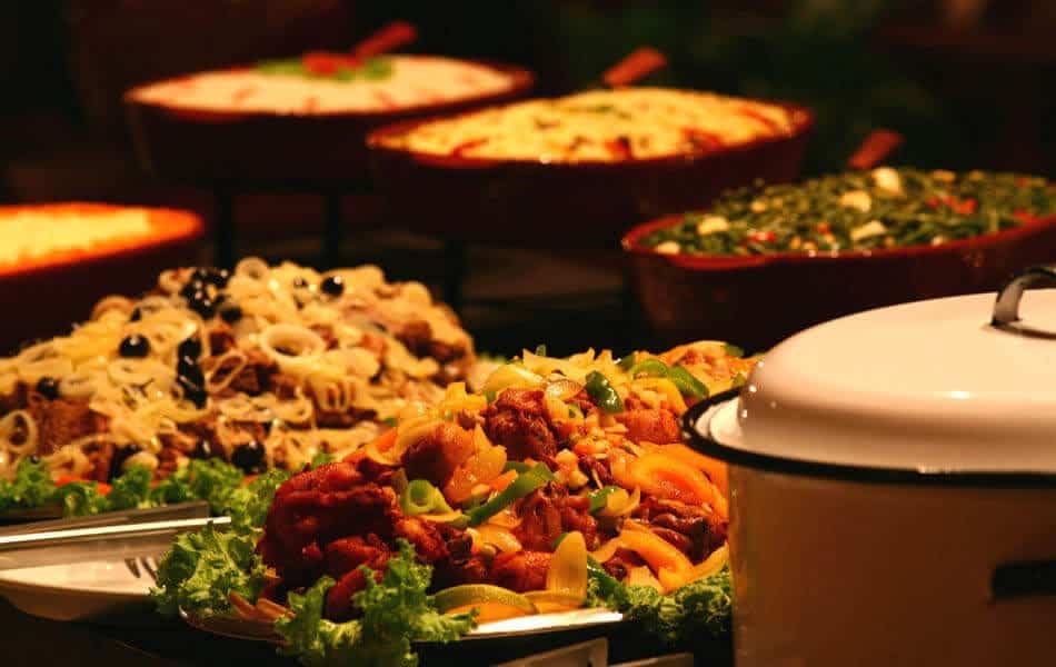 A close-up of a buffet table featuring dishes with vegetables, meats, and garnishes, this scene highlights colorful salads and covered pots—inviting you to experience the vibrant cuisine found among things to do in Guyana, French Guiana, and Suriname.