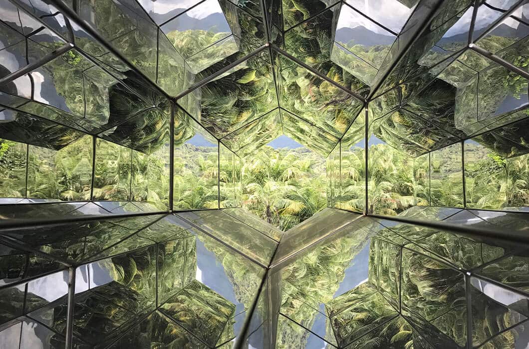 A geometric mirrored structure reflects lush green palm trees and blue sky, creating a kaleidoscopic, symmetrical pattern—an eye-catching scene often found among unique Brazil attractions and perfect for those seeking memorable things to do in Brazil.