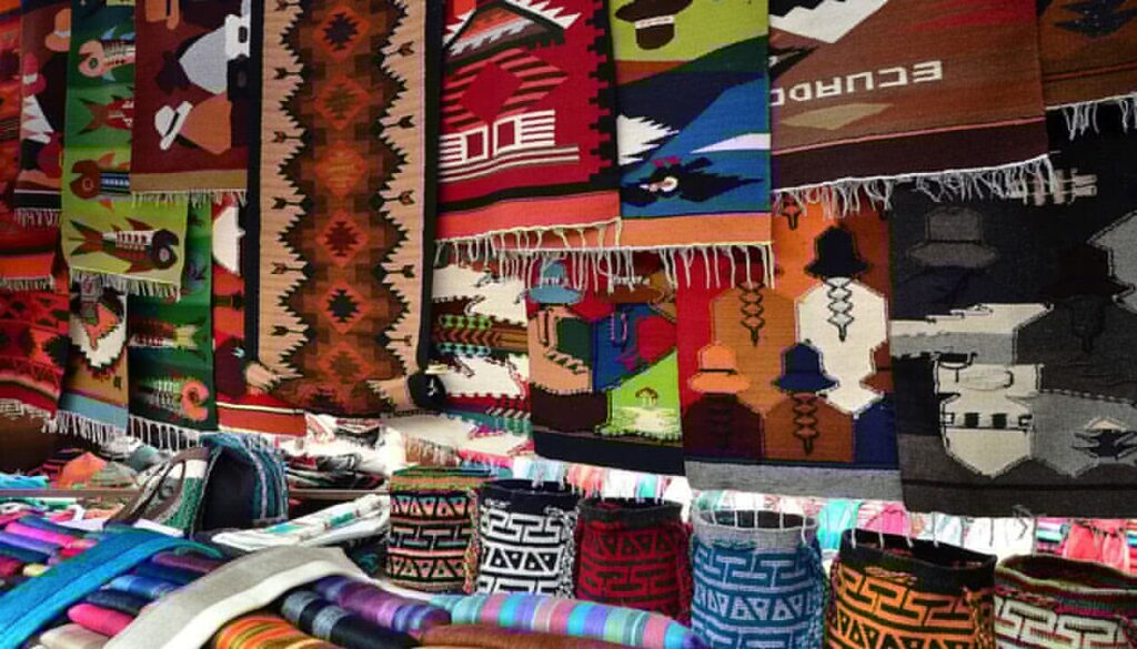 Colorful woven rugs and blankets with intricate patterns and geometric designs hang at a market stall, showcasing vibrant hues—these are must buy souvenirs and perfect South America gifts for anyone who appreciates authentic craftsmanship.