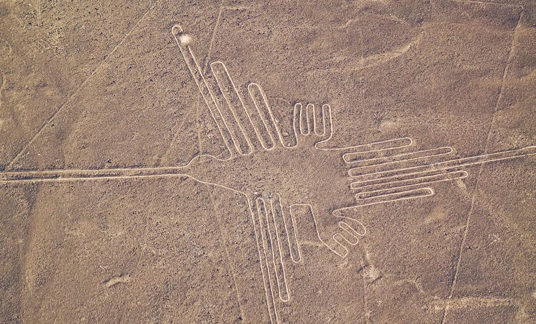 Aerial view of the Nazca Lines in Peru, a must-see Peru attraction, showing a large geoglyph of a hummingbird with long, straight lines forming its wings, beak, and tail—one of the most fascinating things to do in Peru.