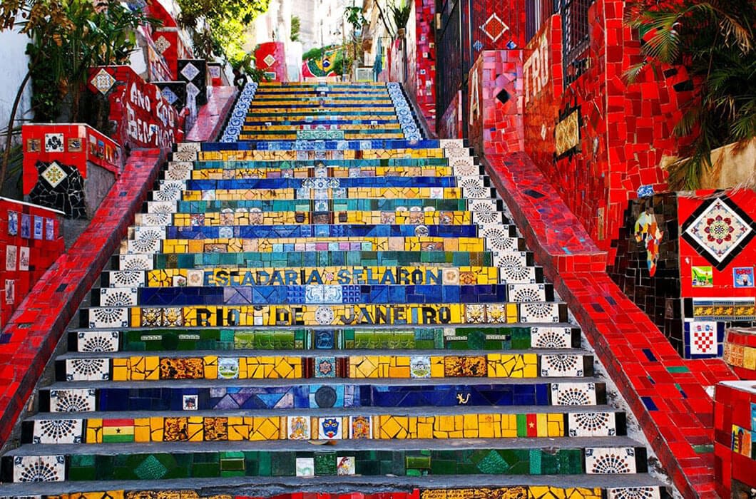 Colorful mosaic-tiled staircase with vibrant red, yellow, green, and blue tiles, the Selarón Steps is a must-see Brazil attraction in Rio de Janeiro, surrounded by tiled walls and lush greenery.