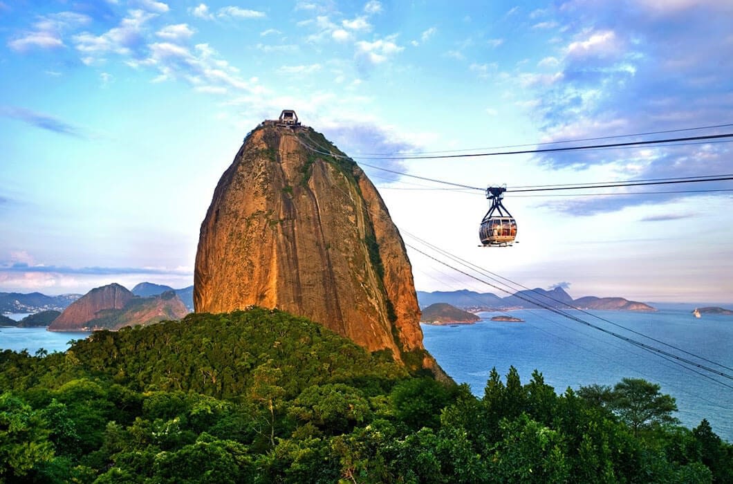 A cable car travels to the top of Sugarloaf Mountain, a highlight among Brazil attractions, offering stunning views of lush greenery, the blue ocean, and distant islands in Rio de Janeiro.