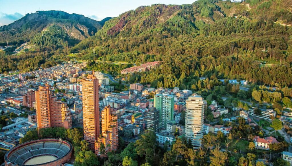 Aerial view of a city with tall buildings and a circular bullring, surrounded by dense green forest and mountains—one of the best places to visit in Colombia for breathtaking scenery and vibrant city life.
