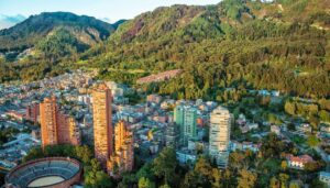 Aerial view of a city with tall buildings and a circular bullring, surrounded by dense green forest and mountains—one of the best places to visit in Colombia for breathtaking scenery and vibrant city life.