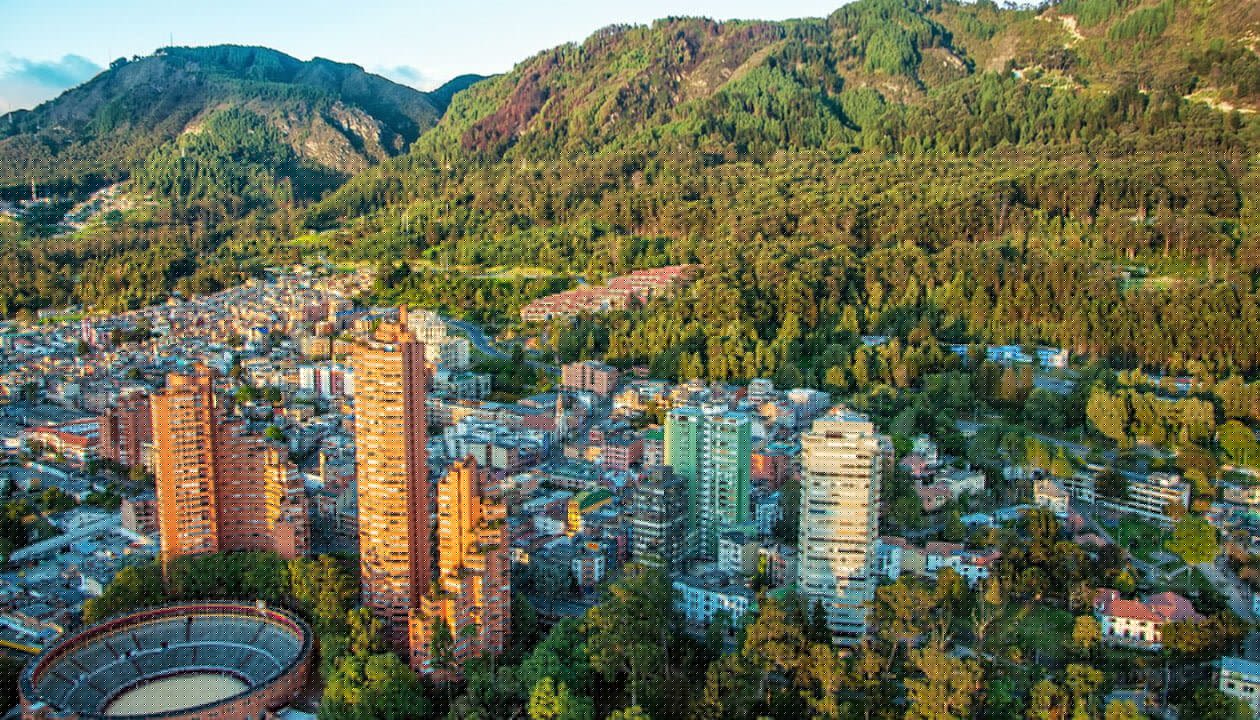 Aerial view of a city with tall buildings and a circular bullring, surrounded by dense green forest and mountains—one of the best places to visit in Colombia for breathtaking scenery and vibrant city life.