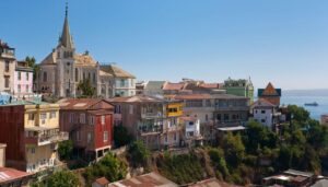 Colorful hillside houses and a church overlook the ocean in Valparaíso, one of the top rated attractions Chile offers. A ship crosses the water as lush greenery surrounds these iconic sights, making Valparaíso a gem of Chile tourism.
