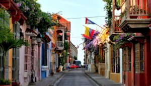 A narrow, colorful street in Cartagena is lined with vibrant colonial buildings, balconies overflowing with flowers, and Colombian flags hanging—one of the top 5 things to see for a lively and inviting atmosphere under a clear sky.