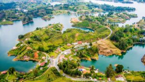 Aerial view of a winding road surrounded by lush green hills, scattered houses, and vibrant blue lakes, showcasing scenic landscapes and the natural beauty celebrated in Colombia tourism.