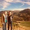 Two people stand side by side, smiling, on a hillside overlooking a scenic valley. The backdrop of green fields and mountains under a partly cloudy sky reflects the serenity and joy that comes from experiencing exceptional service.