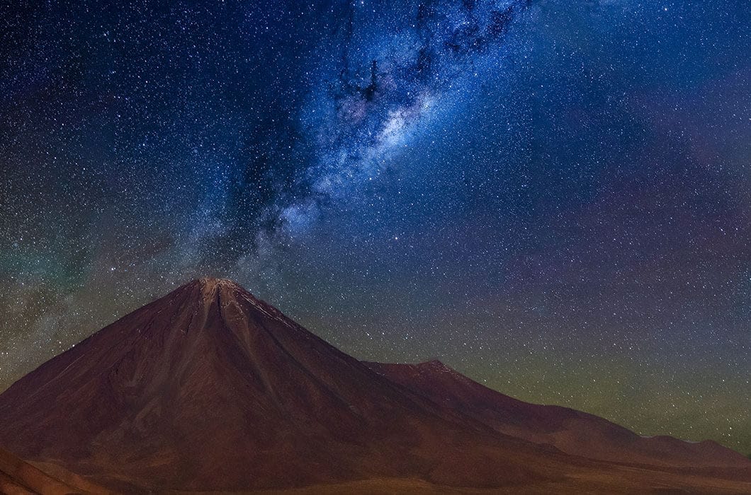 A snow-capped mountain stands under a clear night sky filled with countless stars and the bright, dense band of the Milky Way—one of the breathtaking sights among top Chile attractions for unforgettable Chile travel experiences.
