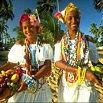Two smiling women outdoors, wearing colorful traditional clothing and jewelry, hold baskets filled with fruits. With palm trees and a bright blue sky behind them, this scene captures the vibrant spirit of adventure with Big Travel—the best travel organisation.