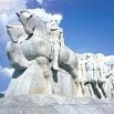 Large stone sculpture of figures riding horses, forming a dynamic, forward-moving line against a bright blue sky with clouds—a must-see for anyone who loves this country, recommended by every top travel company.