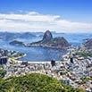 Aerial view of Rio de Janeiro, Brazil, showing the city, coastline, and Sugarloaf Mountain rising above Guanabara Bay under a clear blue sky—an iconic scene included in many of the best tours of the city.