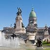 A grand historic building in Buenos Aires with a large green dome, statues, and a fountain in front, set against a clear blue sky.