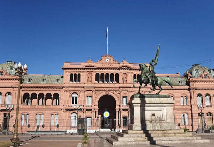A large pink government building with arched windows, a central balcony, and an equestrian statue in front, under a clear blue sky—one of the must-see Argentina attractions for your Argentina travel itinerary.
