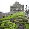 The image shows the Ruins of St. Pauls in Macau, with ornate, symmetrical garden hedges leading up to the historic stone facade under a cloudy sky—a perfect highlight for personalized tours in the city.