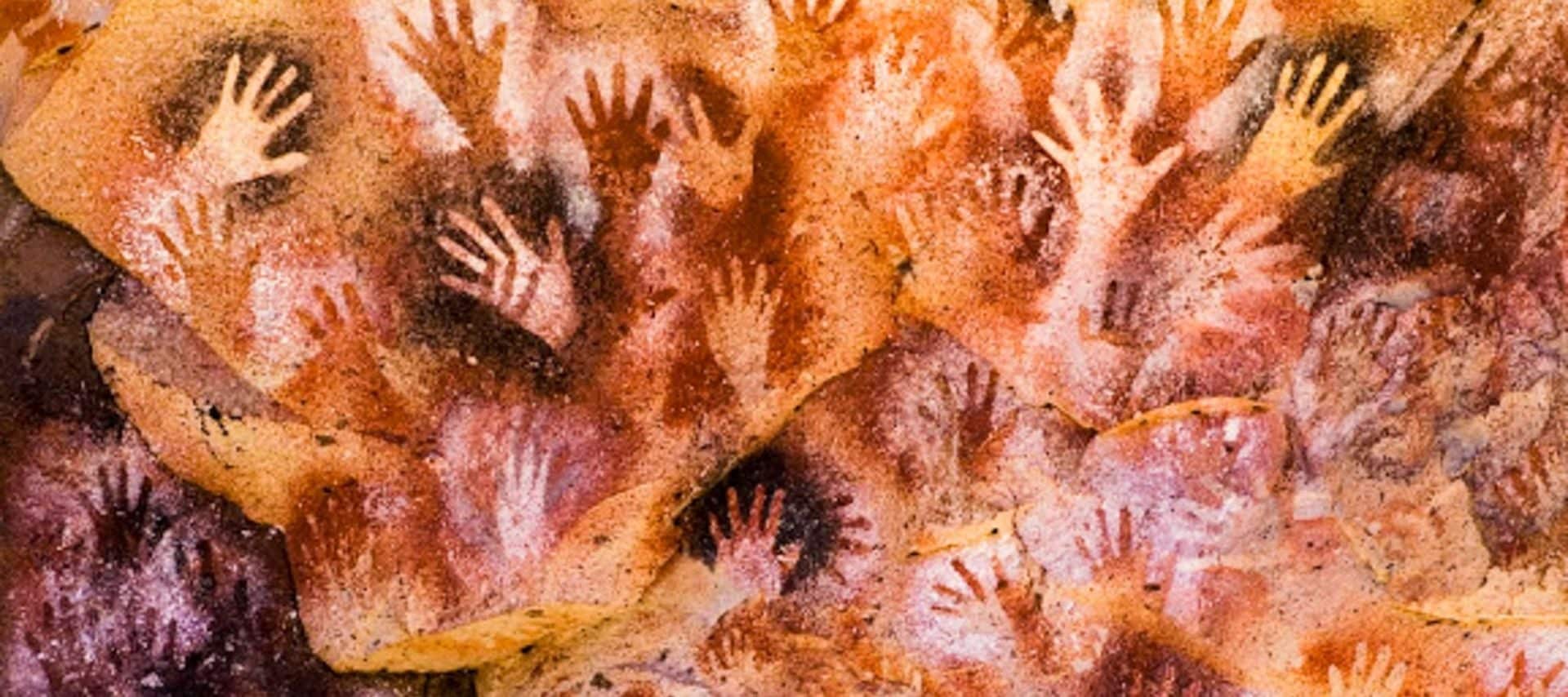 Cave wall covered in overlapping handprints of various sizes, stenciled in shades of brown, red, and white. This striking prehistoric rock art is found in the Cave of the Hands, a highlight for those on Cave of the Hands tours.