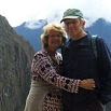 A couple stands close together on a mountain trail in Peru, with rocky cliffs and misty peaks in the background. The woman is smiling, and both are dressed in casual outdoor clothing, enjoying their travel adventure.