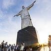 Tourists gather at the base of the Christ the Redeemer statue in Rio de Janeiro, Brazil, creating unforgettable memories as the sun sets and partly cloudy skies paint a stunning background.