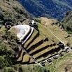 Aerial view of ancient terraced ruins surrounded by lush green mountains, showing stone structures and pathways—an archaeological site where guides offer excellent service to visitors exploring its rich history.