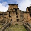Ancient, weathered stone ruins with multiple windows and doorways, surrounded by grass and low stone walls under a partly cloudy sky—a perfect backdrop for a memorable Peru tour or celebrating your first anniversary.