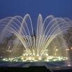A large, illuminated fountain sprays multiple arcs of water upward at night, creating a vibrant display against a dark blue sky—a scene reminiscent of the high service quality that leads to satisfied customers.