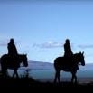 Two people riding horses are silhouetted against a blue sky with distant clouds and mountains, creating a peaceful, scenic outdoor setting—perfect for your next Argentina adventure.