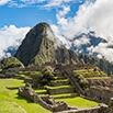 Ancient stone ruins of Machu Picchu with green terraces in the foreground and a large, steep mountain rising behind under a partly cloudy blue sky, promising an unforgettable travel experience.