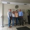 Four people stand close together, smiling for a photo in the lobby of a hotel with a sign reading HOTEL DEL PARQUE on the wall behind them. The setting is bright and welcoming.