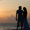 Silhouette of a couple standing close together on a beach during sunset, with the ocean and colorful sky in the background—a perfect scene for a dream honeymoon.
