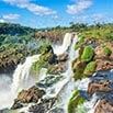 A vibrant waterfall cascades over rocky cliffs surrounded by lush green vegetation under a bright blue sky with scattered clouds, creating the perfect backdrop for memorable moments.