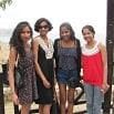 Four young women stand side by side outdoors, smiling at the camera. They look great in their summer outfits, and a wooden fence with a blurry background suggests they are at a scenic location.