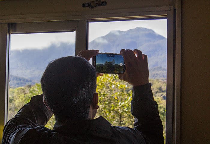A person with short dark hair snaps a photo of a lush, misty mountain landscape through an open window—capturing the essence of South America travel and its breathtaking attractions.