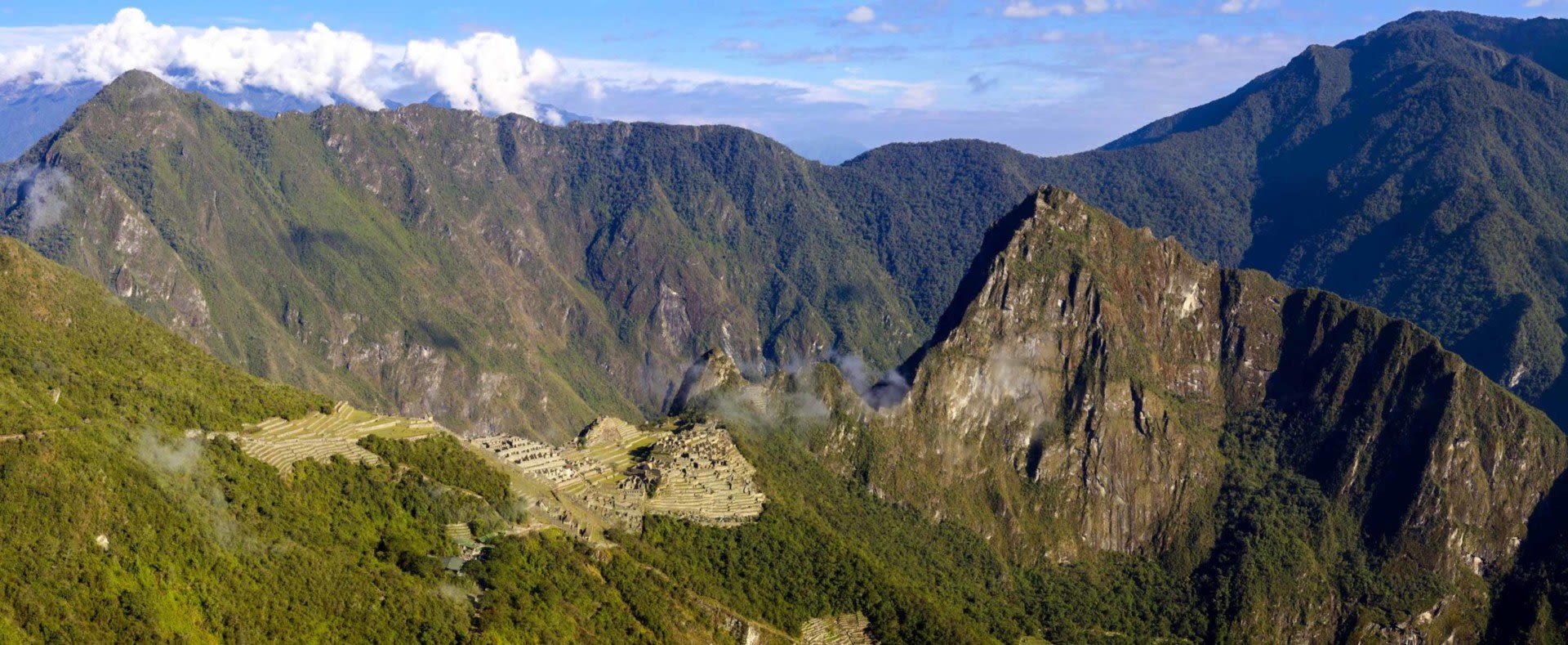 A panoramic view of Machu Picchu’s ancient stone ruins nestled among green mountains under a blue sky captures the allure of Peru travel, inviting adventurers to explore this iconic site in the Andes and check Peru visa requirements before their journey.