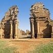 Ancient stone ruins with two large, weathered structures flank a dirt path under a clear blue sky—one of the best natural sights Brazil offers, with more ruins in the background and grass in the foreground inviting exploration.