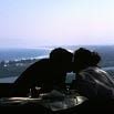 Two people are silhouetted as they kiss at a table by a window, with a scenic view of water and coastline in the bright background—an experience Juliet would highly recommend for its romance and excellent service.