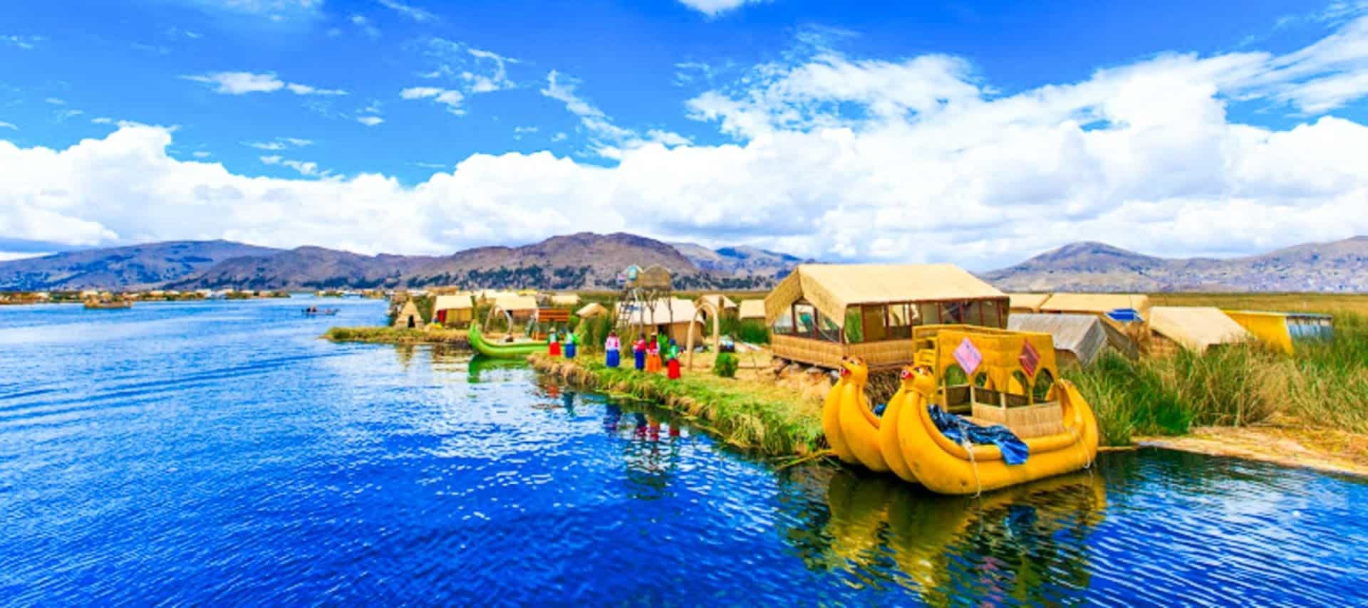 Floating reed islands with thatched huts and colorful boats on a bright blue lake, perfect for Bolivia Cruises, under a sunny sky surrounded by distant mountains and green vegetation.