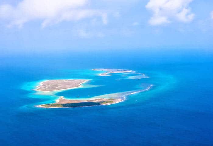 Aerial view of several small, green and sandy islands surrounded by turquoise and deep blue ocean water under a partly cloudy sky—one of the breathtaking Venezuela attractions for those seeking unforgettable things to do in Venezuela.
