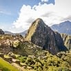 A panoramic view of Machu Picchu in Peru, showing ancient Incan ruins surrounded by lush green mountains with a prominent peak in the background under a partly cloudy sky—an unforgettable family trip destination.