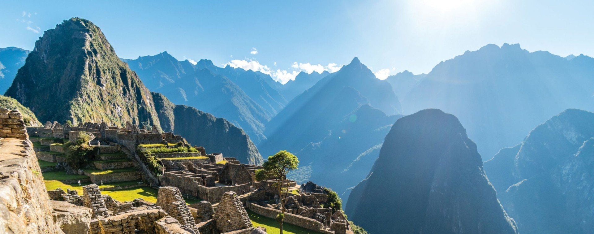 Ancient stone ruins of Machu Picchu sit on a green mountainside under a bright blue sky, inviting travel enthusiasts to explore its wonders—just remember to check visa requirements before embarking on your journey.