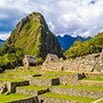 Ancient stone ruins of Machu Picchu in Peru with lush green terraces and a steep mountain peak in the background under a partly cloudy sky.