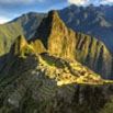 Ancient stone ruins of Machu Picchu sit atop a lush green mountain ridge, with steep peaks and dramatic sunlight—an inspiring sight for any travel planner seeking the ultimate trip planning adventure amid blue skies and distant mountains.