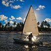 A person sails a small boat on the water, sunlight shining through the sail. Palm trees and a partly cloudy blue sky create a peaceful backdrop—like finding calm after answering questions or offering customer support all day.