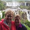 Two women smiling and standing close together in front of large, scenic waterfalls—capturing a travel experience that truly exceeded expectations amid lush greenery.