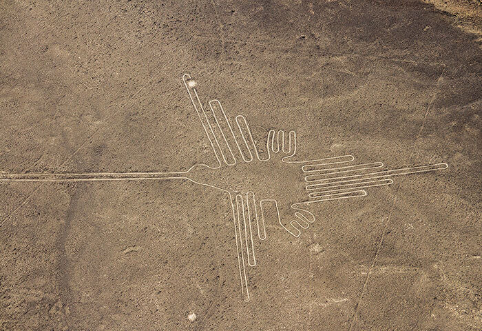 Aerial view of the Nazca Lines in Peru, a must-see South America attraction, showing a large hummingbird geoglyph etched into the desert floor and surrounded by flat, barren land.